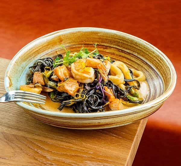 Спагети с морски дарове в керамична купа, представени на дървена маса.